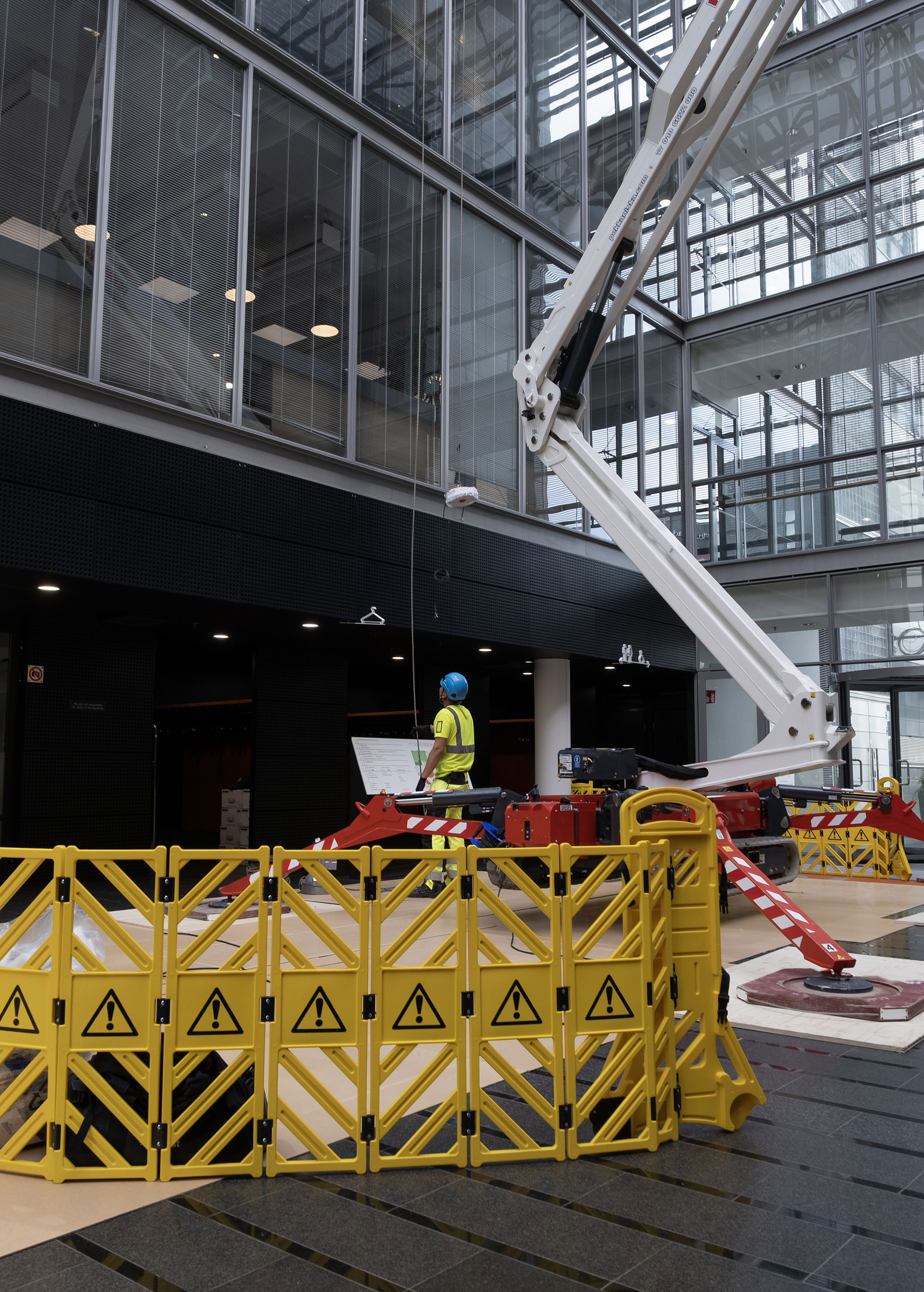 Keltaisen suoja-aidan takana kevytnosturi, jonka vieress&auml; ty&ouml;ntekij&auml; katsoo nosturin nokkaa kohden.